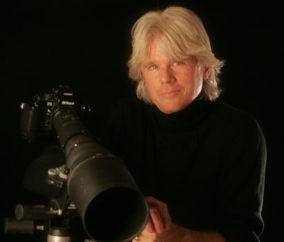 A man holding a camera in front of a telescope.